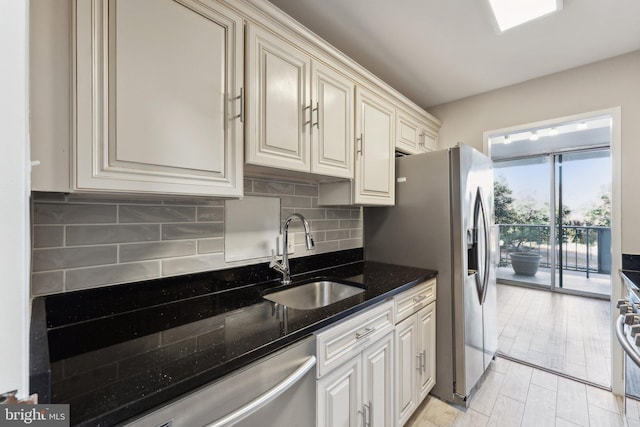 kitchen featuring sink, stainless steel range oven, backsplash, dark stone counters, and cream cabinetry