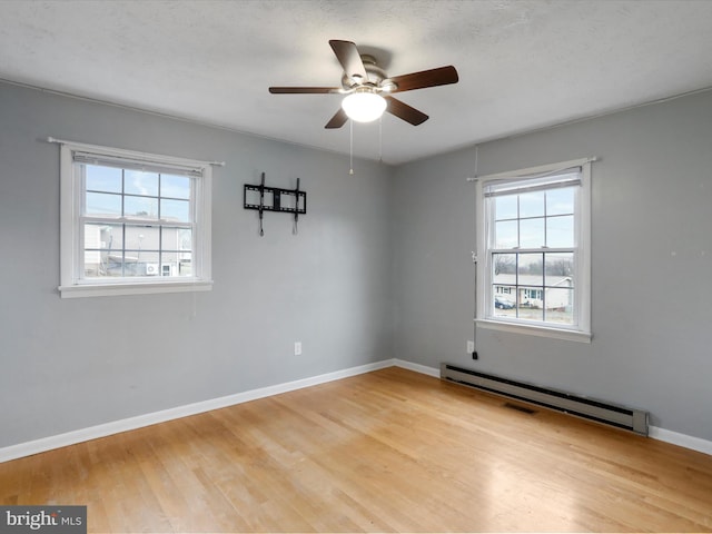 unfurnished room featuring a baseboard radiator, light hardwood / wood-style flooring, ceiling fan, and a healthy amount of sunlight