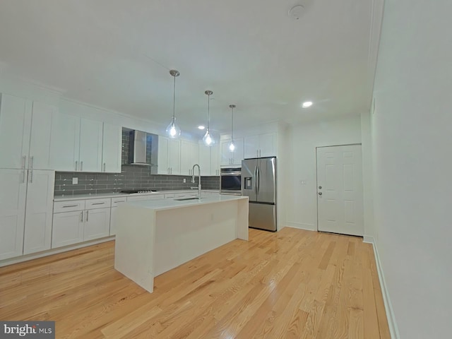 kitchen with white cabinets, wall chimney range hood, light hardwood / wood-style flooring, an island with sink, and stainless steel appliances