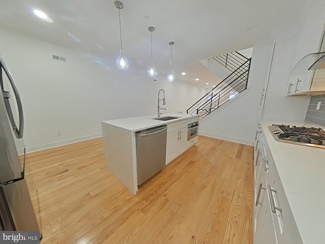 kitchen with white cabinetry, sink, decorative light fixtures, appliances with stainless steel finishes, and light wood-type flooring