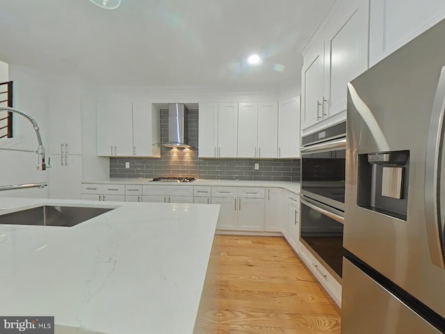 kitchen featuring white cabinetry, wall chimney range hood, tasteful backsplash, light hardwood / wood-style flooring, and appliances with stainless steel finishes