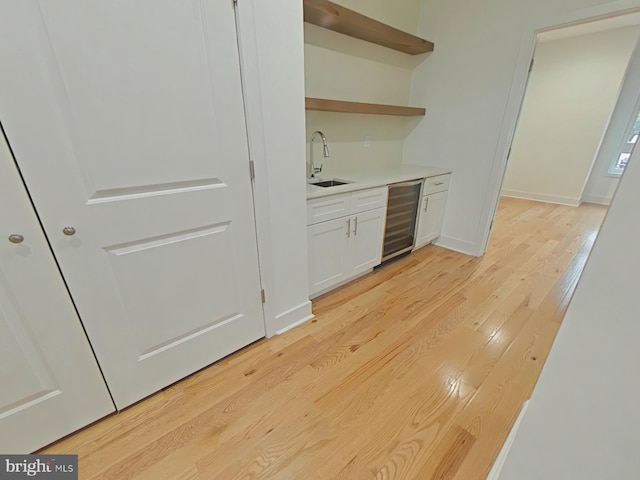 bar with white cabinets, light wood-type flooring, sink, and wine cooler