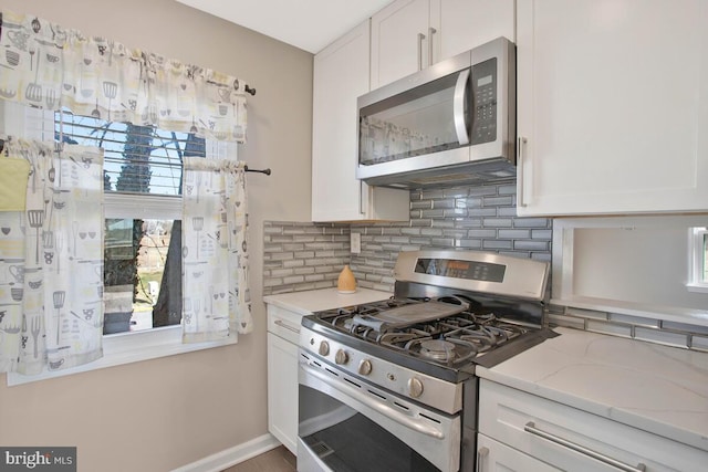 kitchen with white cabinets, light stone counters, backsplash, and appliances with stainless steel finishes