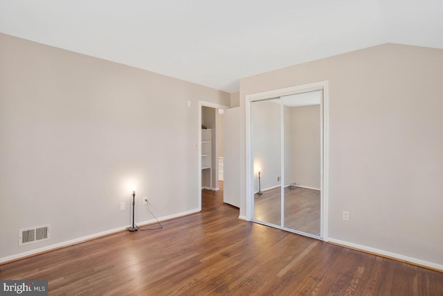 unfurnished bedroom with hardwood / wood-style floors, vaulted ceiling, and a closet