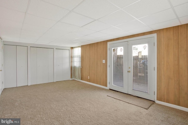 interior space with a paneled ceiling, wooden walls, carpet, and french doors