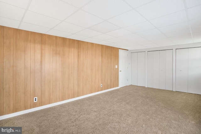 basement featuring carpet flooring, a paneled ceiling, and wood walls