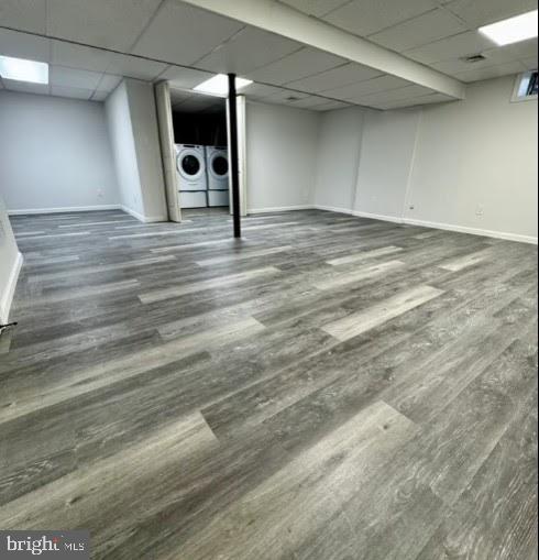 basement with dark hardwood / wood-style flooring, a drop ceiling, and washing machine and clothes dryer