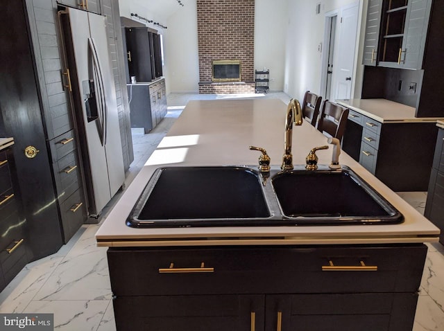 kitchen with a fireplace, stainless steel fridge, a center island with sink, and sink