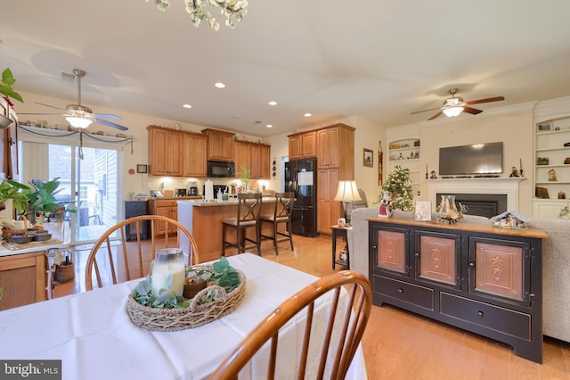 dining area featuring a ceiling fan, a glass covered fireplace, light wood-type flooring, and recessed lighting