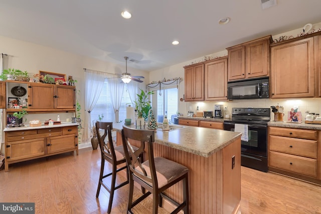 kitchen featuring light wood-type flooring, black appliances, ceiling fan, and a breakfast bar area