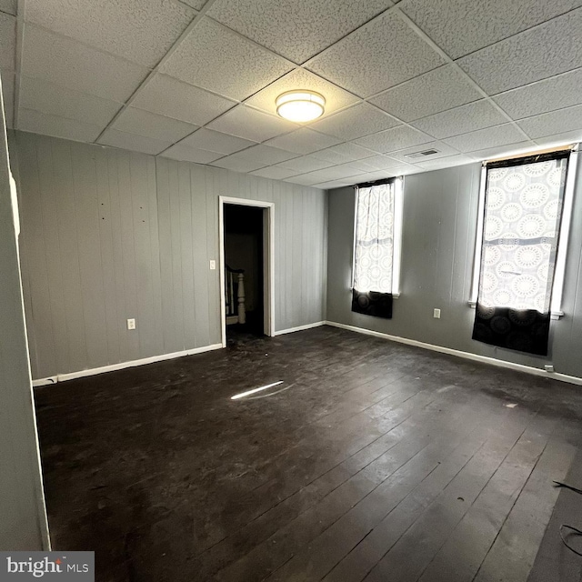 spare room with a paneled ceiling, wooden walls, and dark hardwood / wood-style flooring