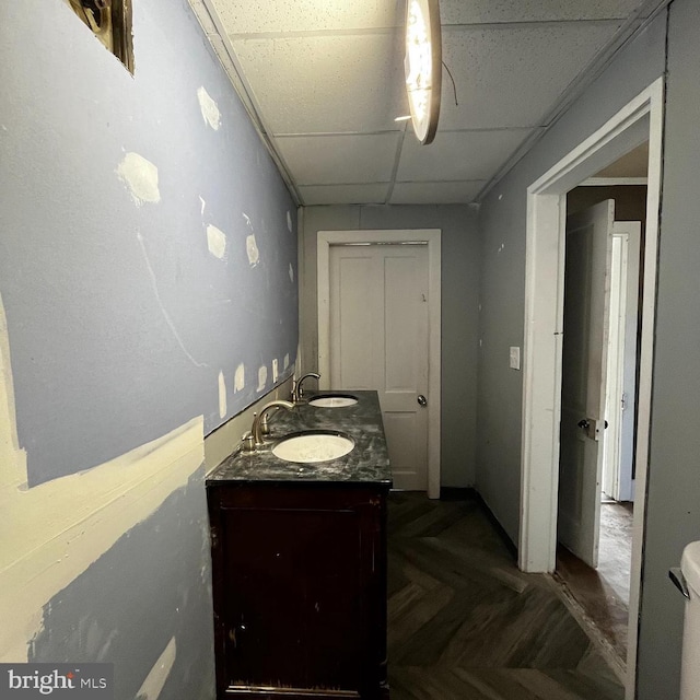 bathroom featuring vanity, a drop ceiling, toilet, and parquet flooring