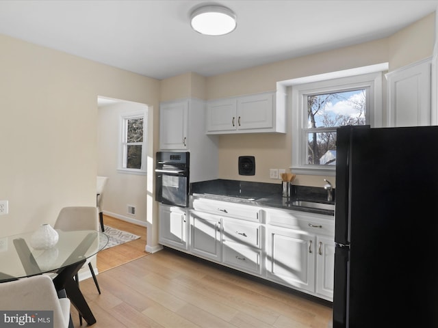 kitchen with sink, white cabinets, black appliances, and light hardwood / wood-style flooring