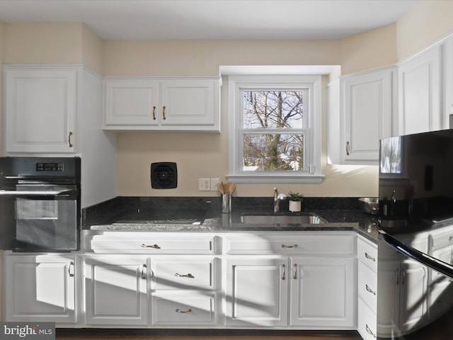 kitchen with black appliances, dark stone countertops, white cabinetry, and sink