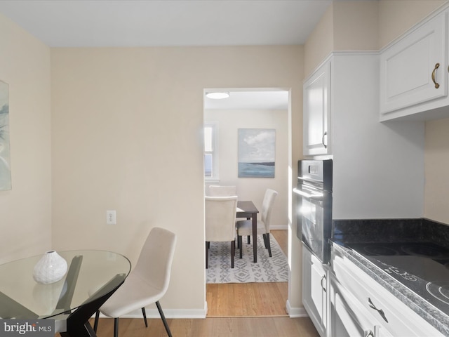 kitchen featuring black oven, stovetop, white cabinetry, and light hardwood / wood-style flooring