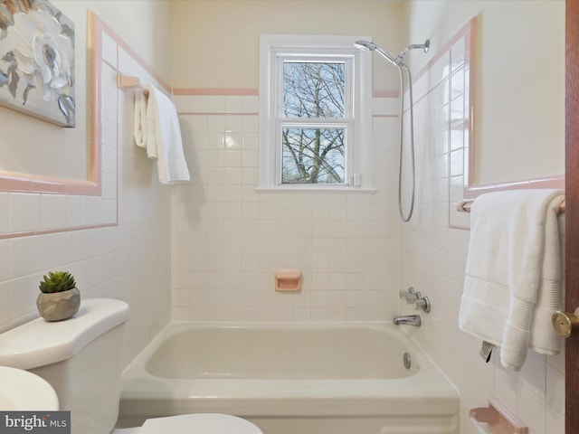 bathroom featuring tiled shower / bath combo, toilet, and tile walls