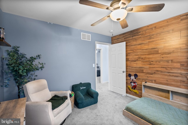 living area with light carpet, ceiling fan, and wooden walls