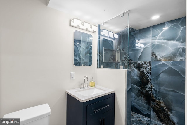 bathroom with a tile shower, vanity, and toilet