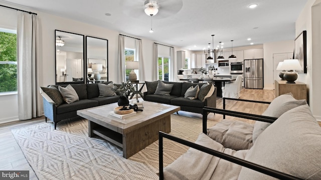 living room with ceiling fan with notable chandelier and light hardwood / wood-style floors