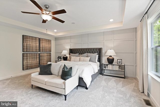 bedroom with light colored carpet, a raised ceiling, and ceiling fan