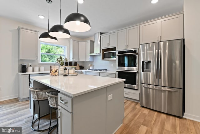 kitchen with wall chimney exhaust hood, stainless steel appliances, a kitchen breakfast bar, decorative light fixtures, and a kitchen island