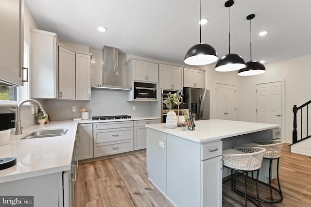 kitchen featuring appliances with stainless steel finishes, sink, wall chimney range hood, light hardwood / wood-style floors, and a kitchen island