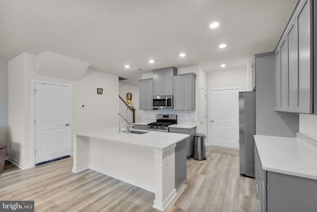 kitchen featuring decorative backsplash, appliances with stainless steel finishes, gray cabinets, light hardwood / wood-style floors, and an island with sink