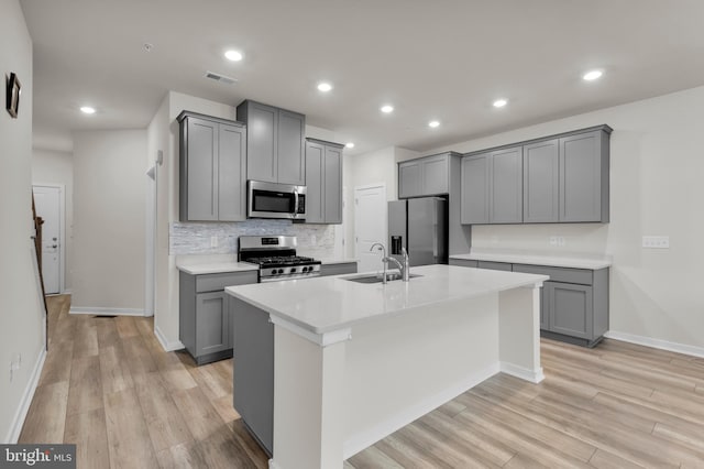 kitchen featuring gray cabinets, sink, an island with sink, and appliances with stainless steel finishes