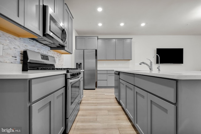 kitchen with light wood-type flooring, stainless steel appliances, gray cabinetry, and backsplash