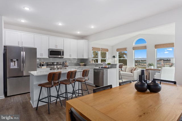 kitchen with dark wood-type flooring, vaulted ceiling, appliances with stainless steel finishes, a kitchen island, and white cabinetry