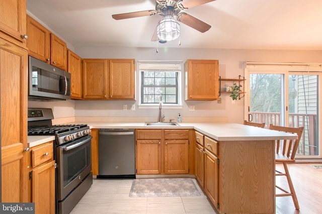 kitchen with kitchen peninsula, appliances with stainless steel finishes, a breakfast bar, ceiling fan, and sink