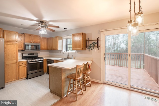 kitchen with pendant lighting, a breakfast bar, sink, appliances with stainless steel finishes, and kitchen peninsula