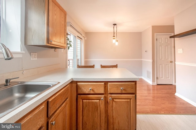 kitchen with kitchen peninsula, light hardwood / wood-style flooring, decorative light fixtures, and sink