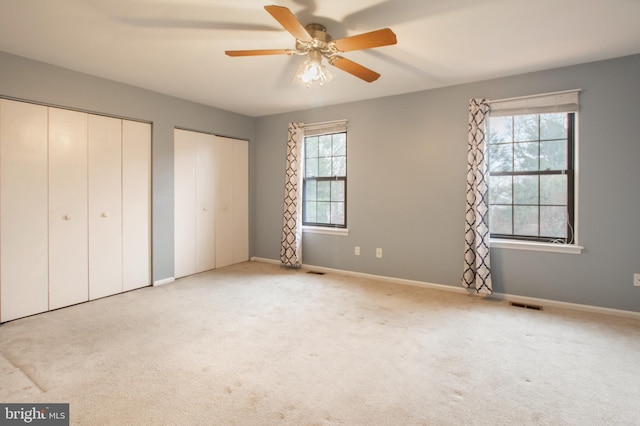 unfurnished bedroom featuring light carpet, multiple windows, multiple closets, and ceiling fan