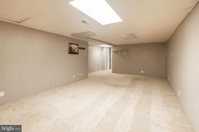 basement with a paneled ceiling, wood walls, and light colored carpet