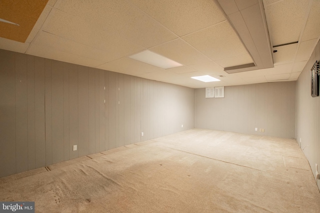 basement featuring a drop ceiling, carpet floors, and wooden walls