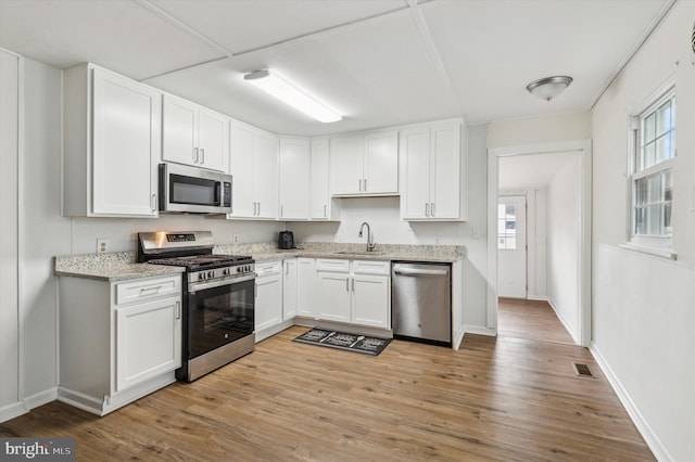 kitchen featuring sink, light hardwood / wood-style flooring, light stone countertops, white cabinetry, and stainless steel appliances