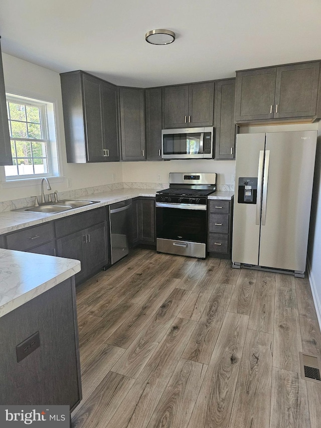 kitchen featuring appliances with stainless steel finishes, light hardwood / wood-style flooring, dark brown cabinets, and sink