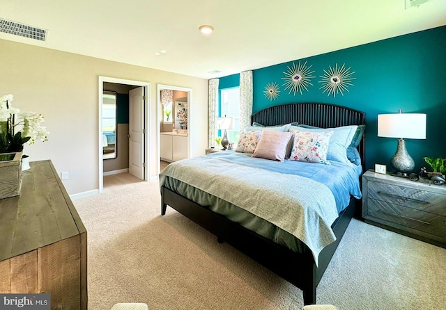 bedroom with light colored carpet, multiple windows, and ensuite bath