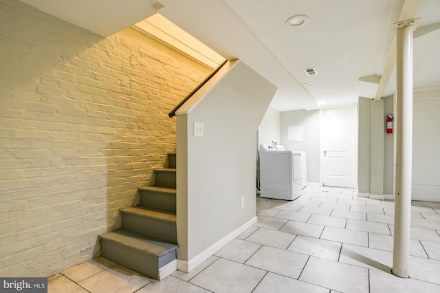 stairway featuring tile patterned flooring, brick wall, and independent washer and dryer