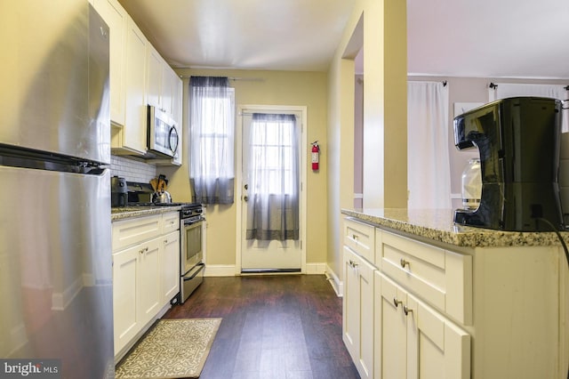 kitchen with light stone countertops, white cabinetry, dark wood-type flooring, tasteful backsplash, and appliances with stainless steel finishes