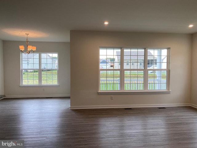 spare room featuring dark wood-type flooring and an inviting chandelier