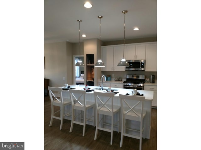 kitchen featuring stainless steel appliances, dark wood-type flooring, pendant lighting, white cabinetry, and an island with sink