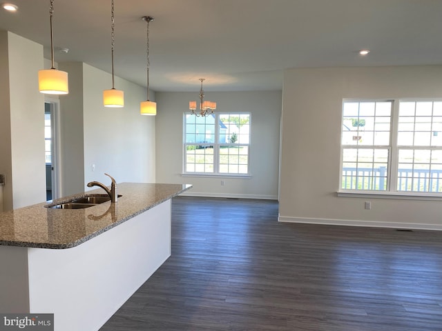 kitchen featuring sink, dark hardwood / wood-style flooring, a notable chandelier, dark stone countertops, and pendant lighting