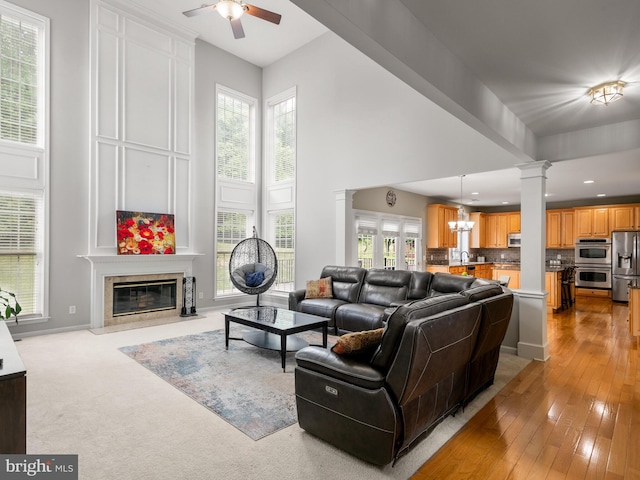 living room featuring plenty of natural light, light hardwood / wood-style floors, ceiling fan with notable chandelier, and a tiled fireplace