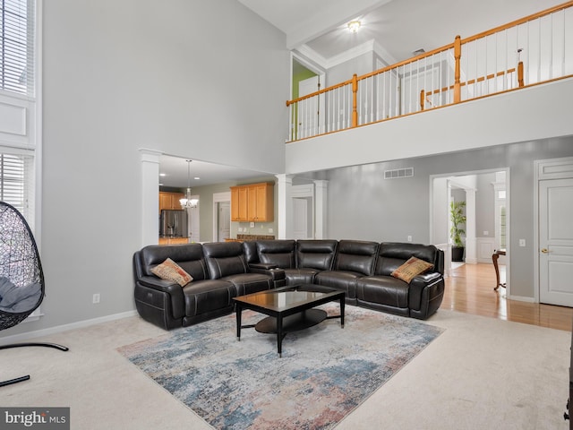 living room featuring light colored carpet, ornate columns, a high ceiling, and an inviting chandelier