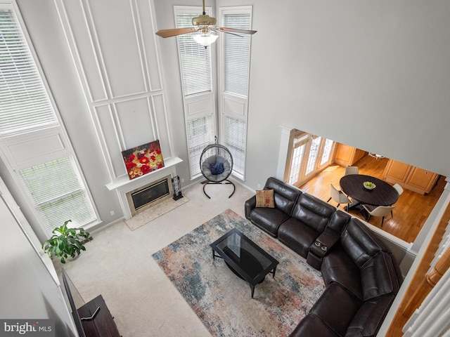 carpeted living room with ceiling fan and a high ceiling