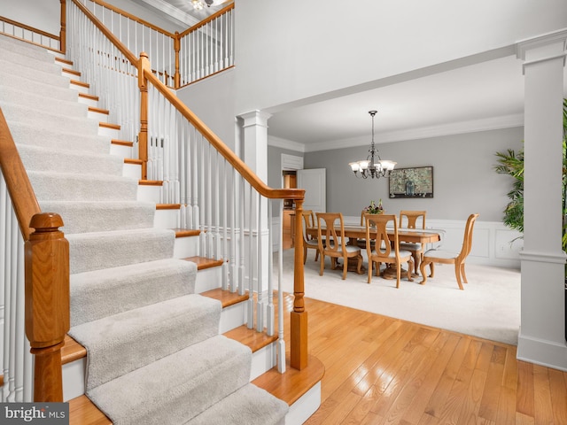 stairway with hardwood / wood-style flooring, crown molding, and a notable chandelier