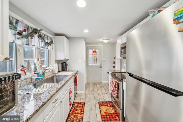 kitchen featuring white cabinetry, light stone countertops, light wood-type flooring, and appliances with stainless steel finishes