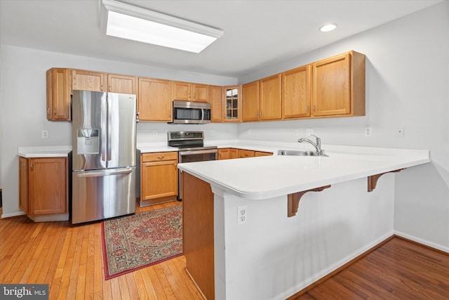 kitchen featuring sink, light hardwood / wood-style flooring, kitchen peninsula, a breakfast bar area, and appliances with stainless steel finishes